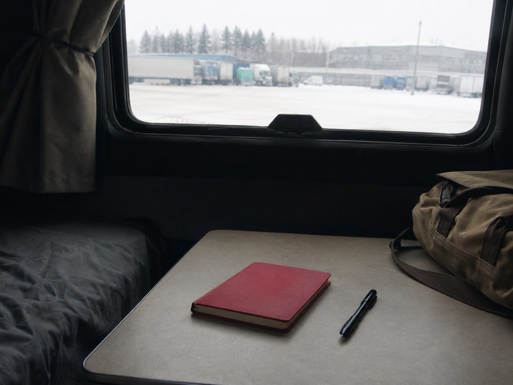 A red notebook resting inside a parked truck cab, with snow outside
