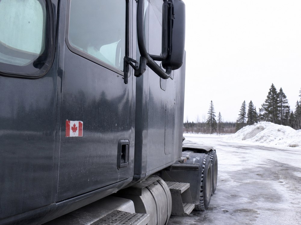 A Canadian flag on a grey truck beside a snowy yard